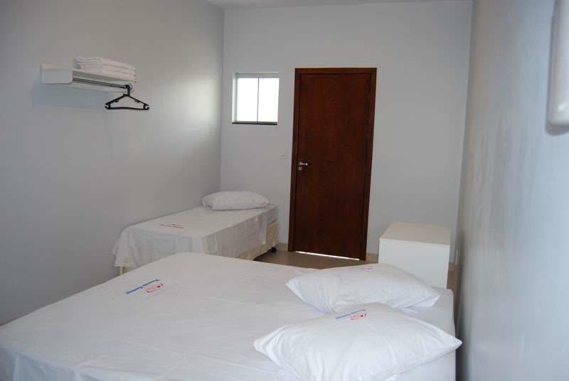 Quarto com camas arrumadas, janela e porta de madeira